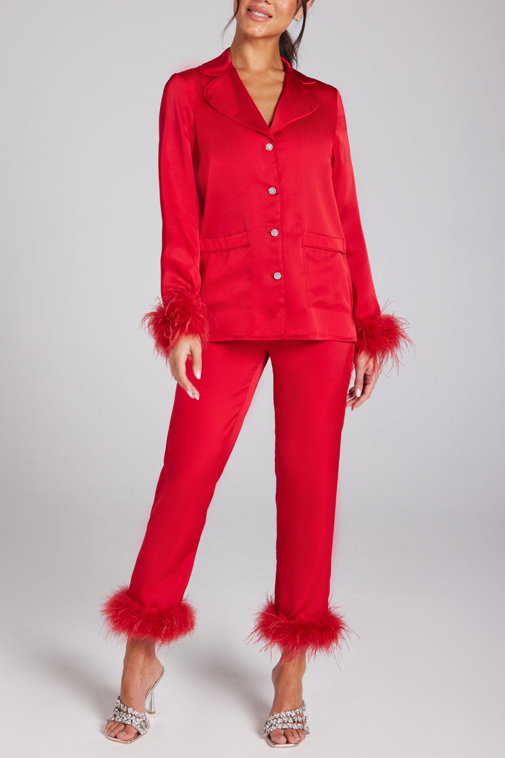 A model wearing red satin pajamas with diamant-encrusted buttons and feather detailing on the shirt and trouper cuffs.